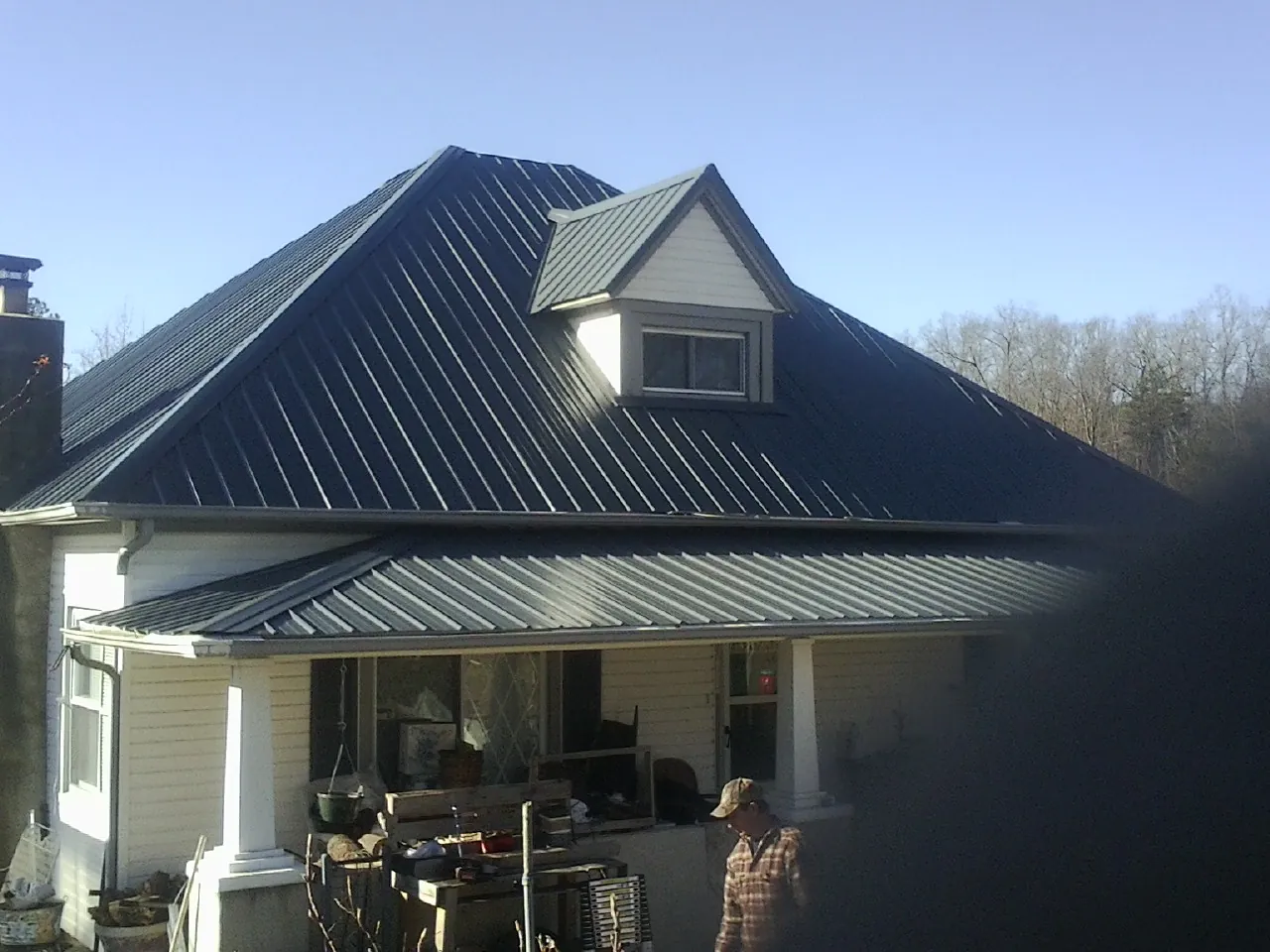 Dark blue standing seam metal roof with a dormer above a front porch in Lyons